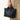 A person holds a black pebbled leather Small Yore Tote Bag by Songmont with gold hardware.