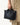 A person holds a black pebbled leather Small Yore Tote Bag by Songmont with gold hardware.