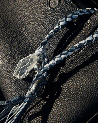 Tranquil Crystal Charm with moonstone crystal, silver bead, and braided blue & white cord on black leather bag.