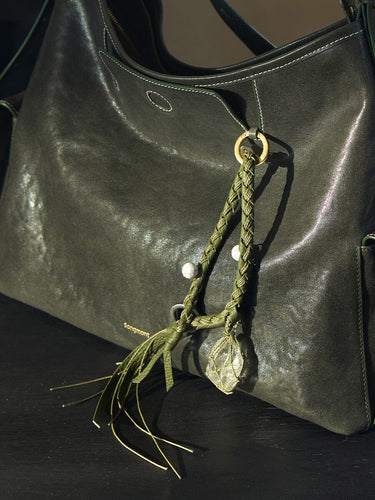 Olivine Tranquil Crystal Charm with braided leather, turquoise beads, and raw crystal on a dark green leather bag.