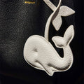 White vegan leather whale charm on black Songmont bag. Made from recycled ocean plastic.
