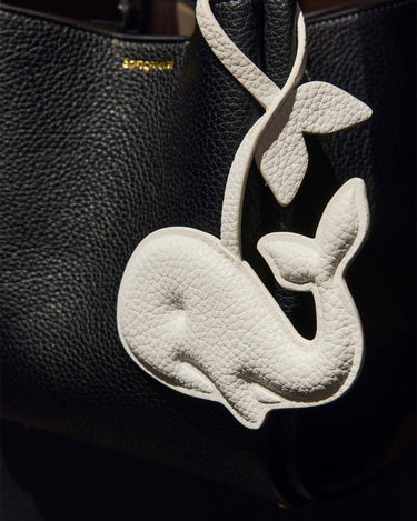 White vegan leather whale charm on black Songmont bag. Made from recycled ocean plastic.
