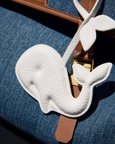Vegan Charm whale accessory made of white vegan leather on a brown strap, on denim.
