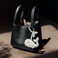 Black vegan leather handbag with a white whale charm, made from recycled ocean plastic.
