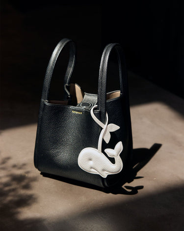 Black vegan leather handbag with a white whale charm, made from recycled ocean plastic.