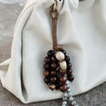 Caramel Wish Seeds Charm with assorted bodhi seeds and stone beads, attached to a leather loop on a cream bag.