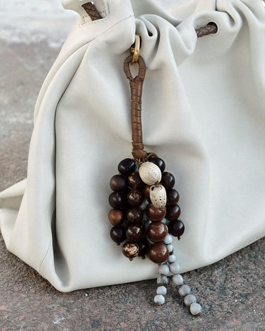 Caramel Wish Seeds Charm with assorted bodhi seeds and stone beads, attached to a leather loop on a cream bag.