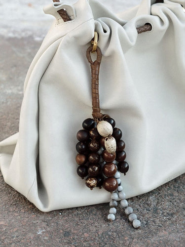 Caramel Wish Seeds Charm with assorted bodhi seeds and stone beads, attached to a leather loop on a cream bag.