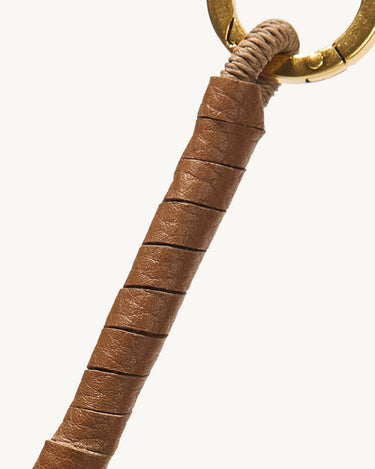 Caramel leather-wrapped charm with a gold ring and braided cord.