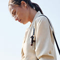 Wish Seeds Charm in denim color, featuring natural Bodhi seeds and a leather cord, attached to a woman's light jacket.