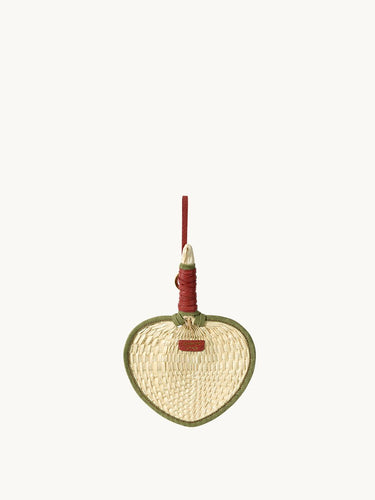 Woven fan charm with green trim and red handle, crafted from palm fronds